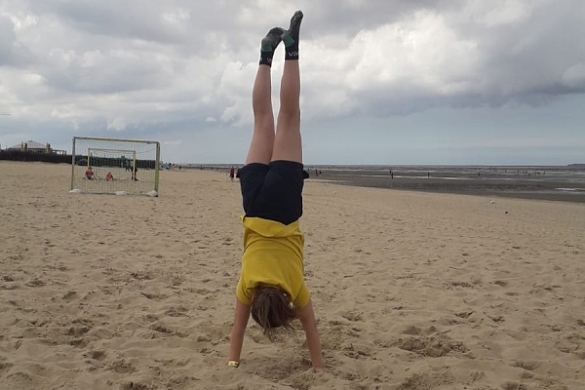 Bild eines Kindes, das einen Handstand am Strand macht