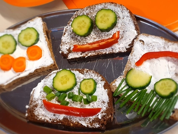 Bild eines Brots mit Frischkäse und buntem Gemüse welches als Gesicht angeordnet ist